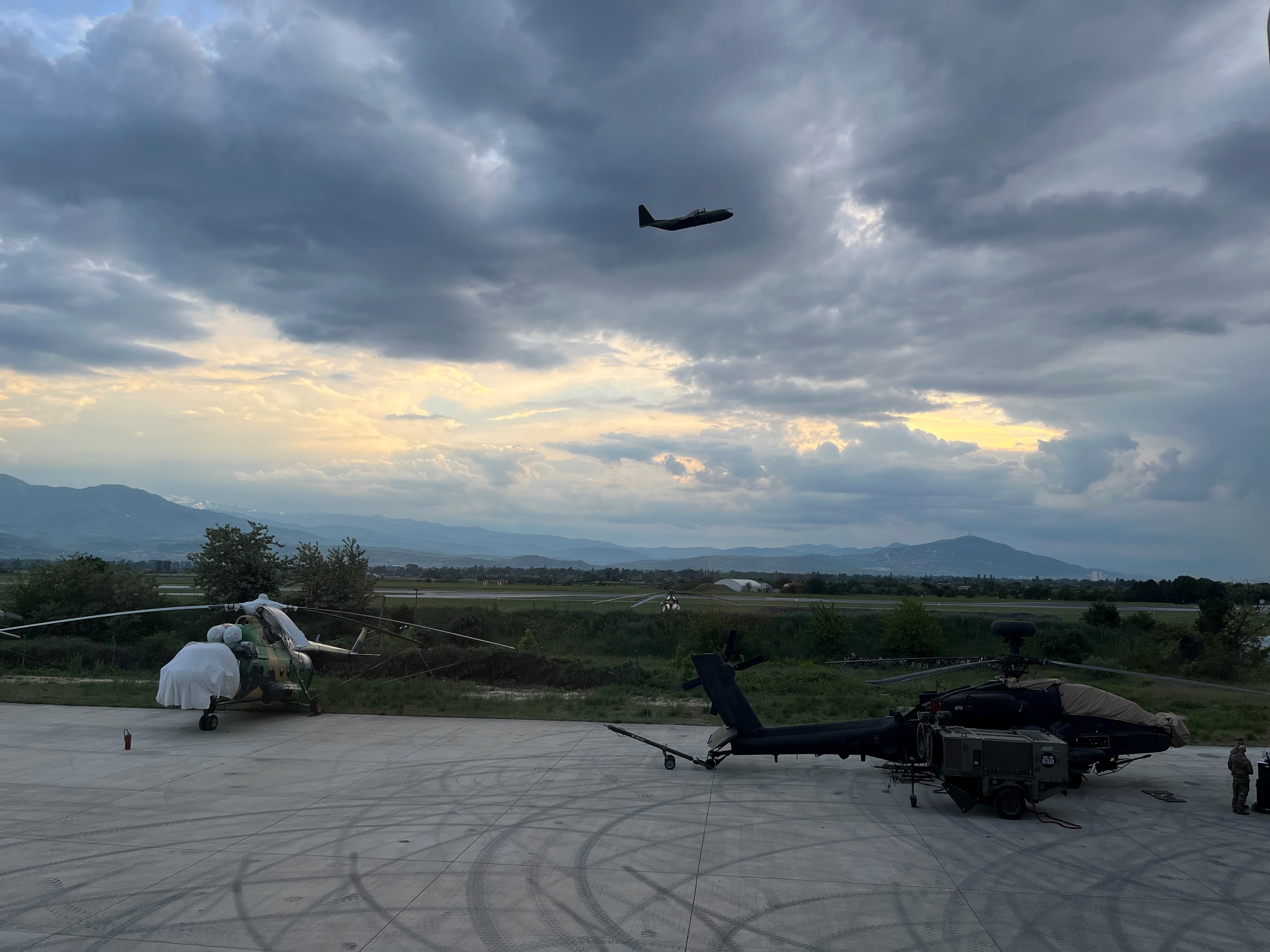 Helicopters on airfield while a Hercules in flight.